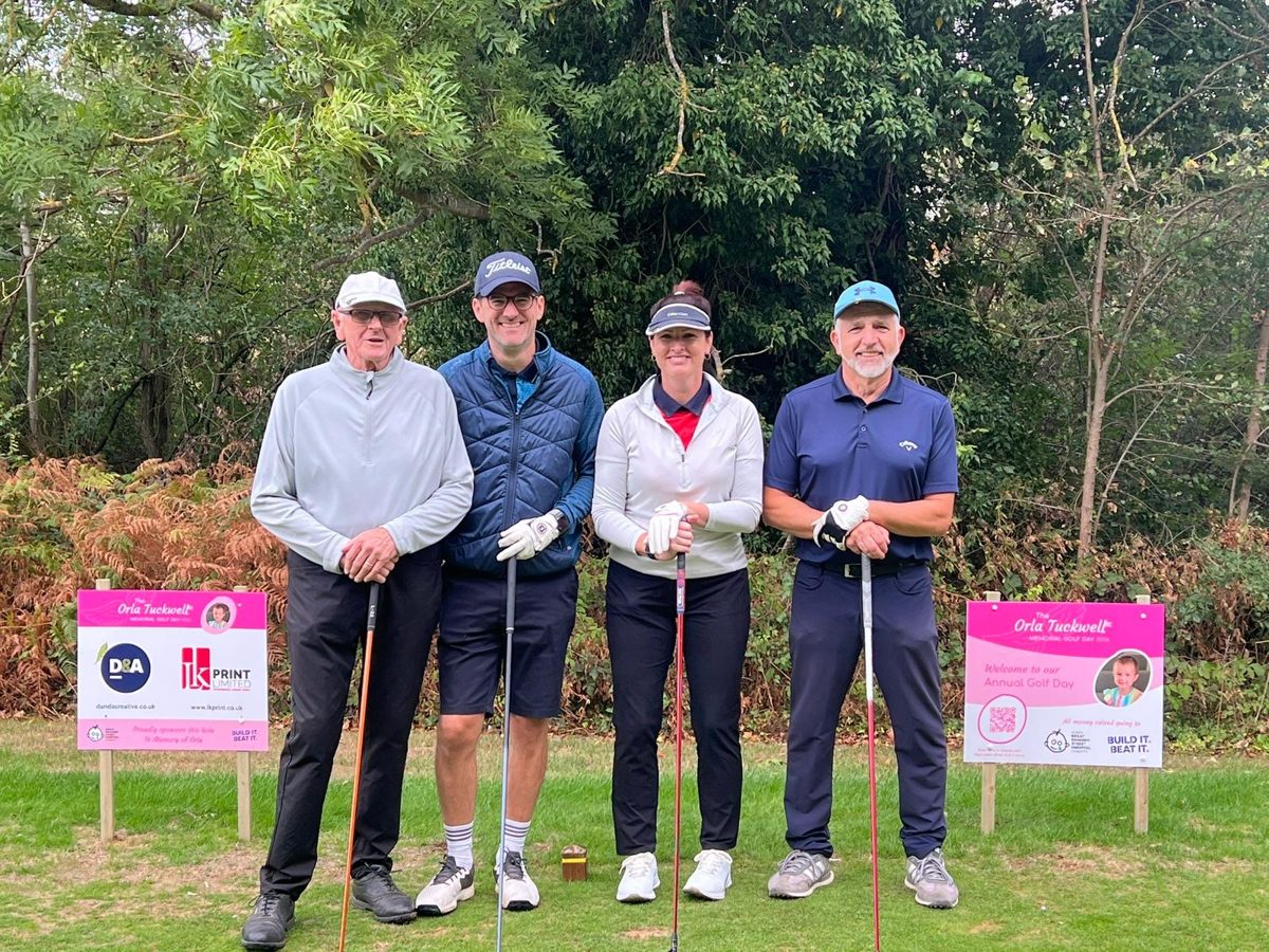 A team of four golfers on the tee beside Orla Tuckwell Memorial Golf Day signs